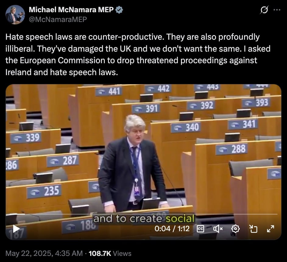 Video still of a man in a suit speaking in a large parliamentary chamber with numbered seats, discussing hate speech laws in the UK and Ireland.